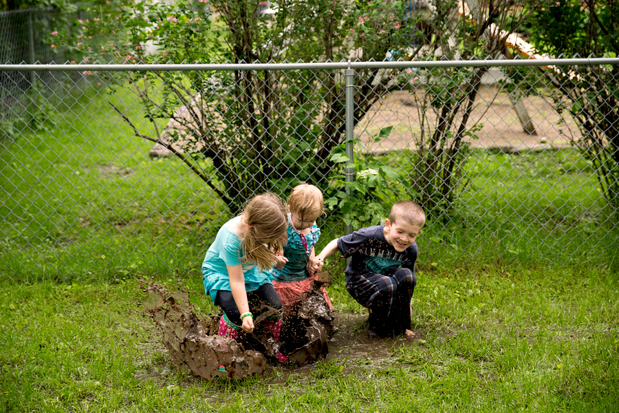three kids jumping in a giant mud puddle
