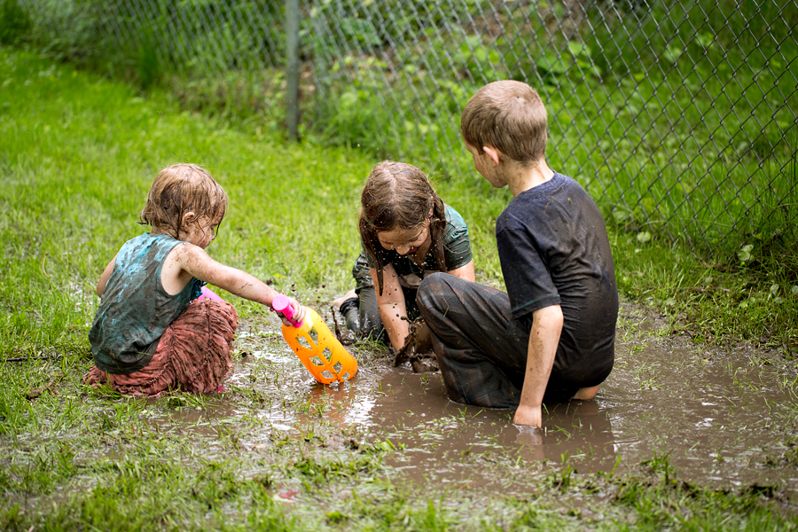 three kids playing in a backyard mud puddle
