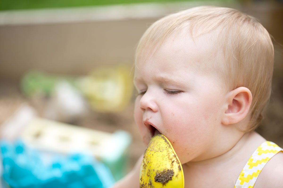 baby shovels sand in her mouth