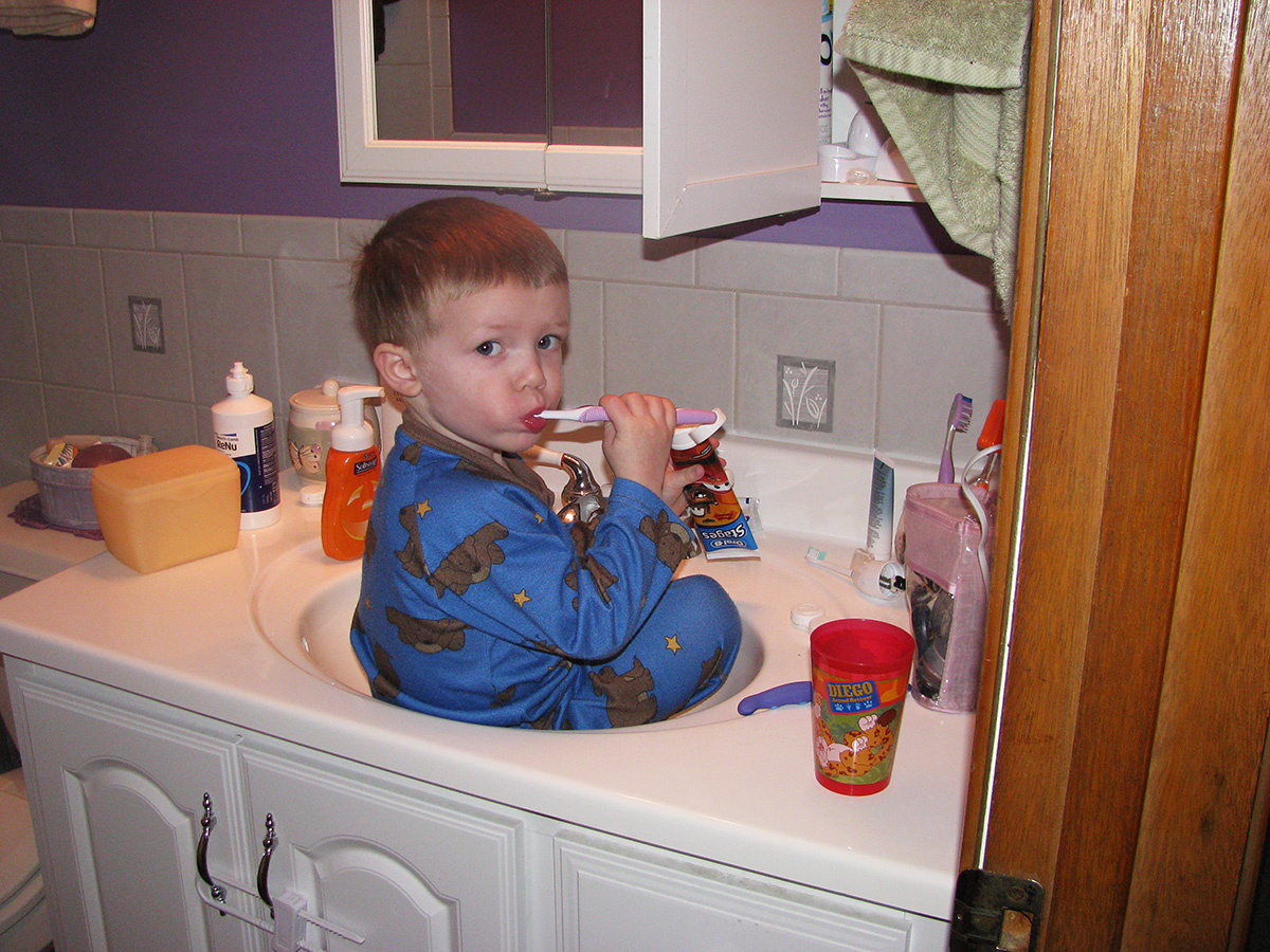 Three year old brushing with mom's toothbrush